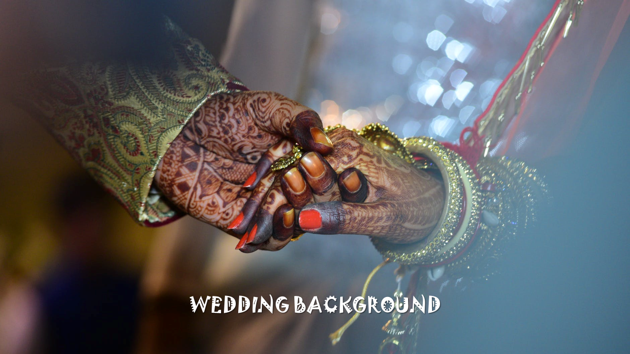 A bride and groom holding hands, decorated with henna and wearing traditional wedding attire, with a soft background.