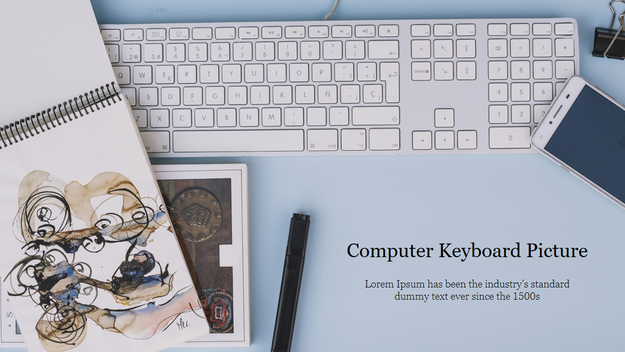 Top view of a white computer keyboard with a notebook, pen, smartphone, and binder clip on a light blue desk.